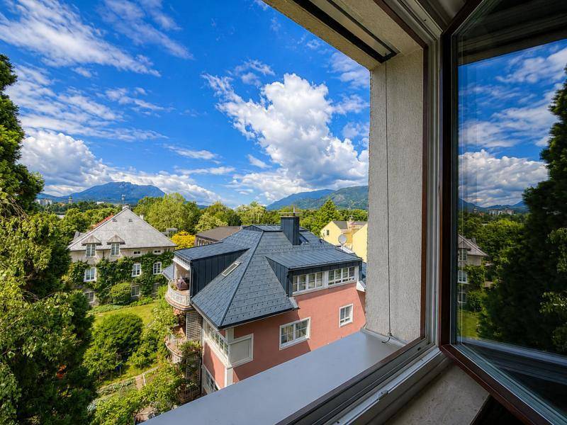 Ausblick aus dem Fenster auf charmante Wohnhäuser, üppiges Grün und die umliegende Berglandschaft.