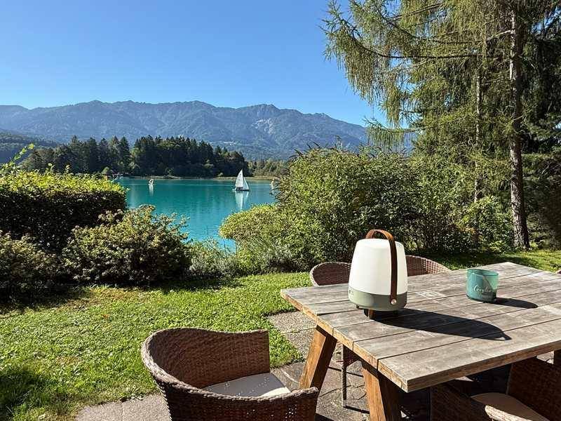 Gemütlicher Essbereich im Freien mit Holztisch und Stühlen, umgeben von Grün und Seeblick.