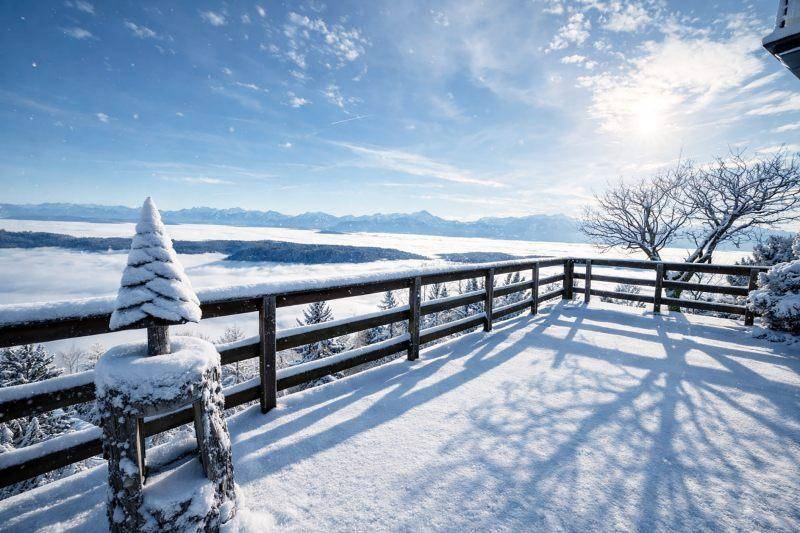 Große, verschneite Aussichtsterrasse mit Holzgeländer und spektakulärem Blick auf die Bergwelt.