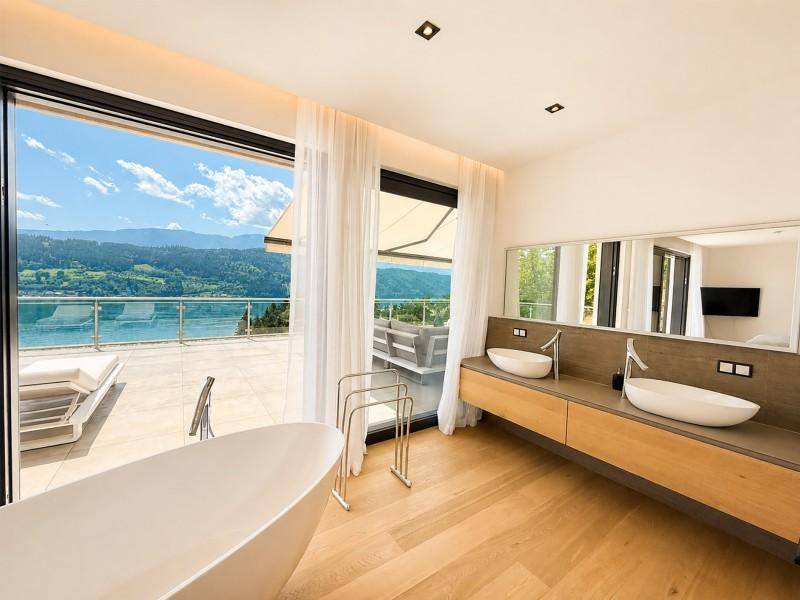 Modernes Badezimmer mit freistehender Badewanne, Doppelwaschbecken und raumhohen Fenstern mit Seeblick.