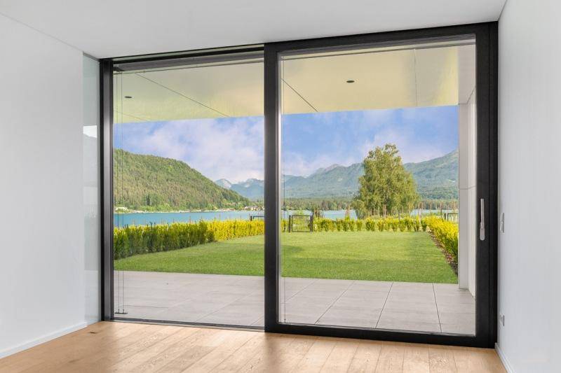 Heller Innenraum mit großen Schiebetüren, die einen weiten Blick auf den See und die Berge bieten.