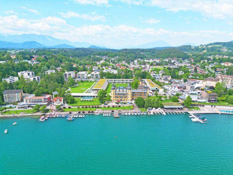 Luftbild einer Küstenstadt mit einem großen Hotelkomplex, Bootsanlegestellen und Bergen.