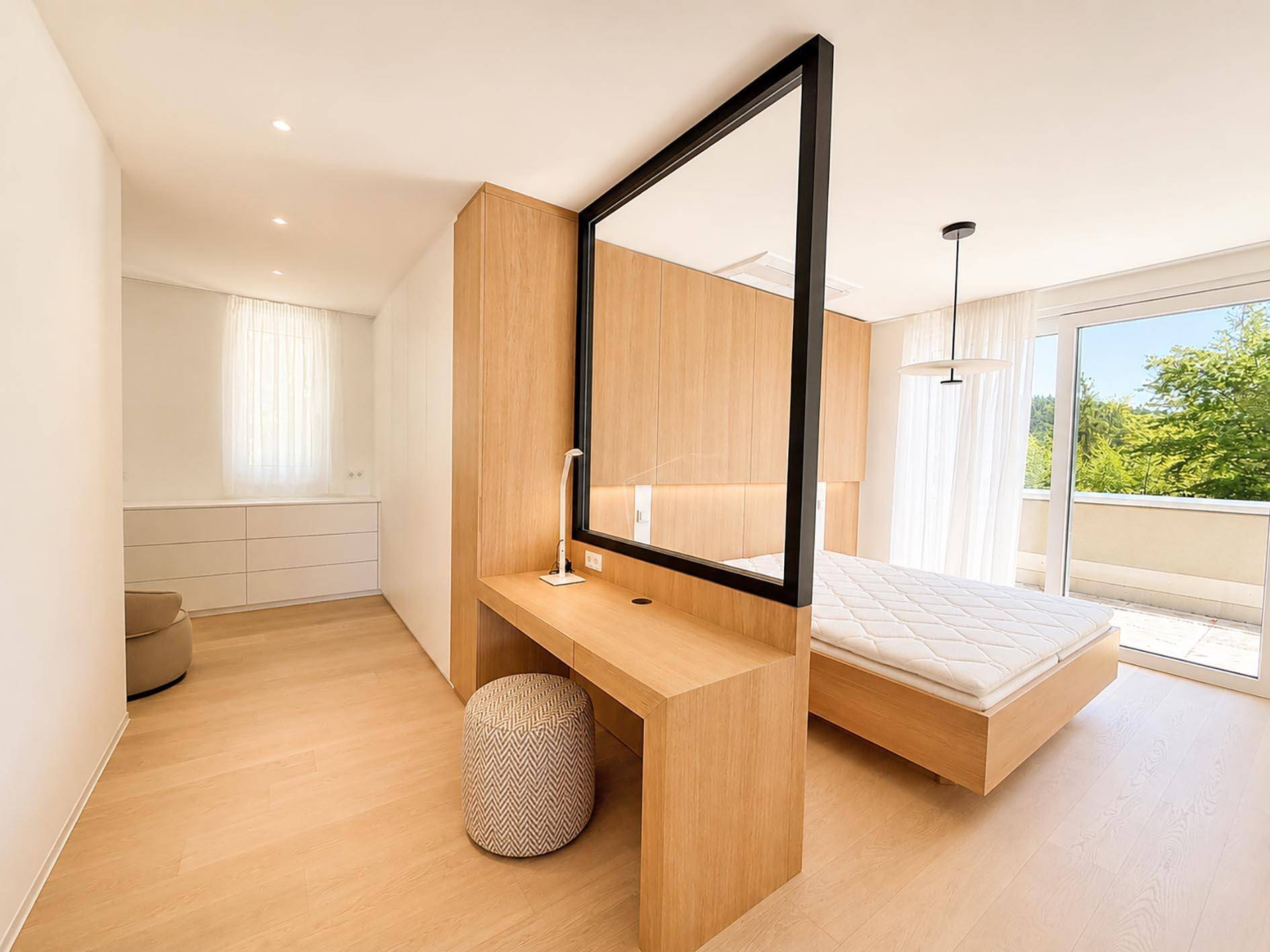 Helles Schlafzimmer mit Holzboden, integriertem Schreibtisch und Zugang zu einem Balkon.