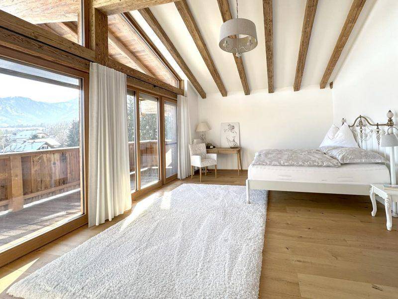 Gemütliches Schlafzimmer mit Balkonzugang, Holzbalken und weitem Blick auf die umliegende Bergwelt.