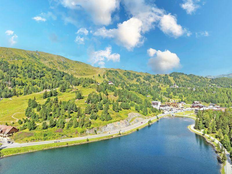 Panoramablick auf einen großen See neben einer Straße, umgeben von einem Dorf und grünen Bergen.