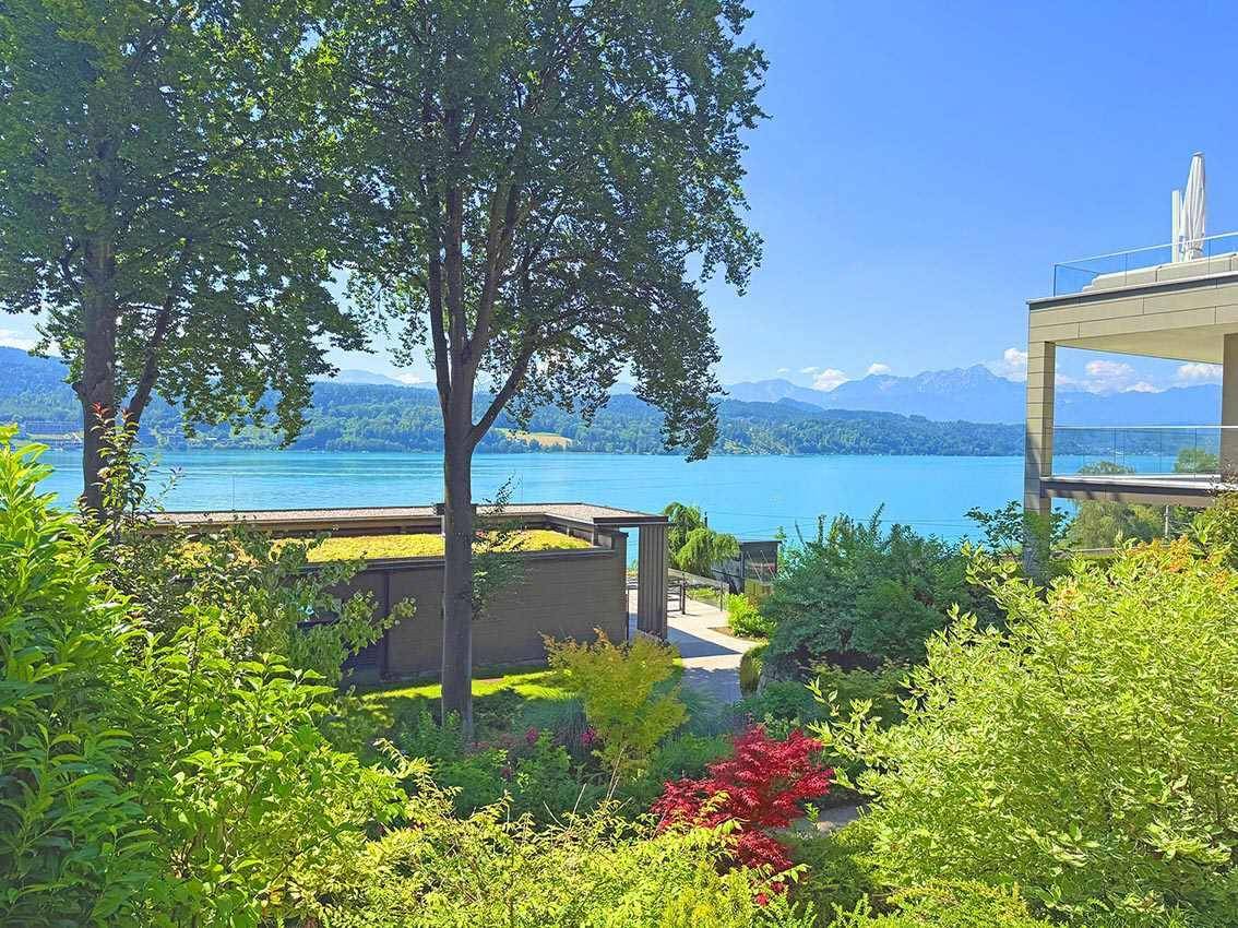 Gepflegter Gartenbereich mit üppiger Vegetation und atemberaubendem Blick auf den See und die umliegenden Berge.