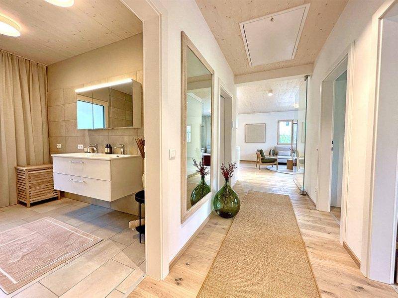 Modernes Badezimmer mit Doppelwaschbecken und Spiegelschrank, angrenzend an einen hellen Flur.