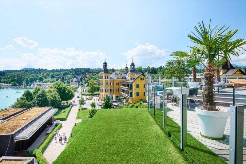 Grüne Dachterrasse mit Kunstrasen, Palmen und weitem Blick auf die Stadt und den See.