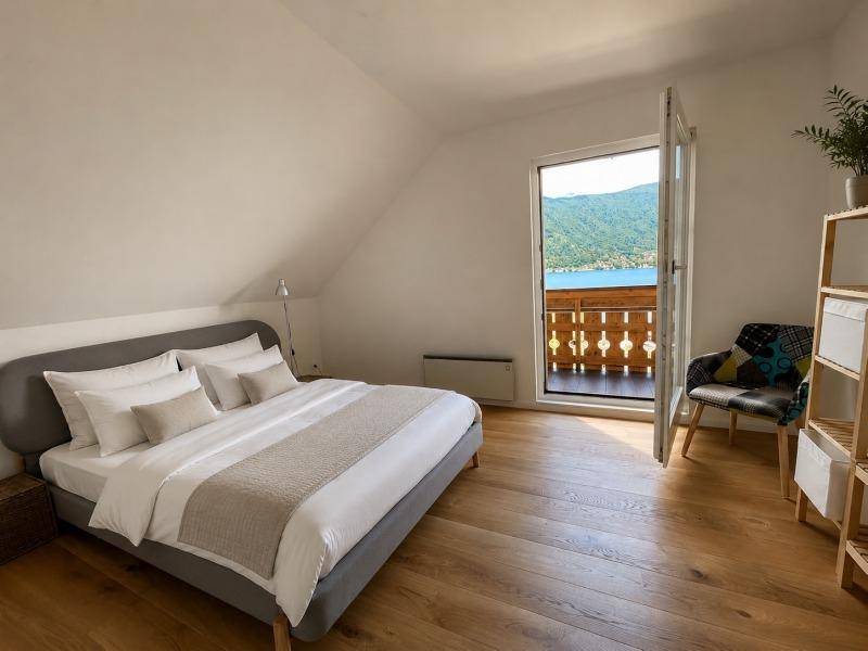 Gemütliches Schlafzimmer mit Holzboden und Balkonzugang, bietet einen malerischen Blick auf den See.