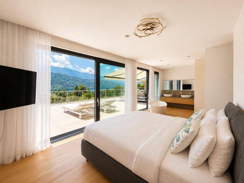 Elegantes Schlafzimmer mit Seeblick, Zugang zur Terrasse und offenem Badbereich mit freistehender Badewanne.