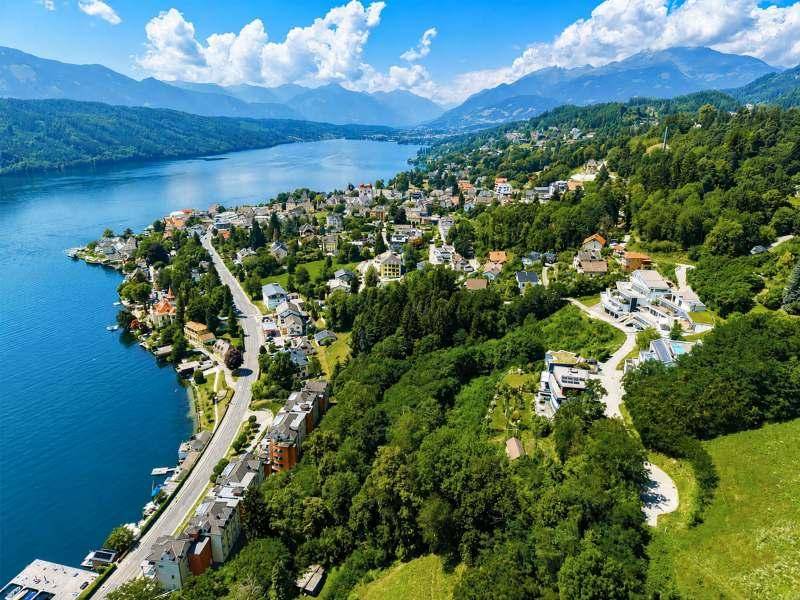 Malerische Luftaufnahme einer Siedlung am Seeufer, umgeben von grünen Hügeln und majestätischen Bergen.