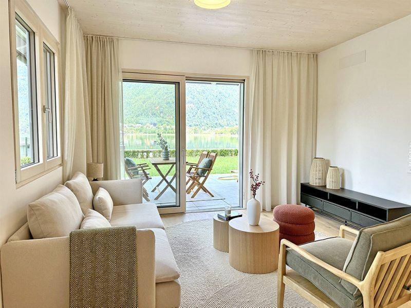 Gemütliches Wohnzimmer mit Sofa, Teppich und direktem Zugang zur Terrasse mit Seeblick.