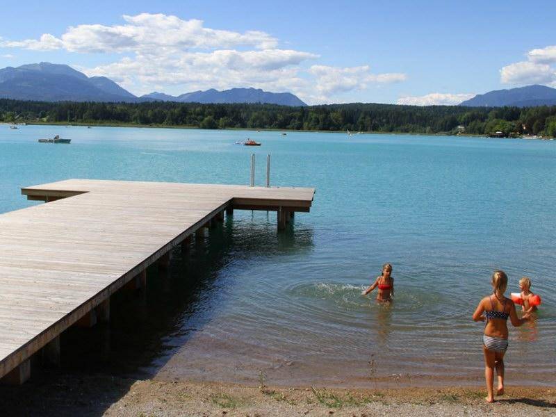 Kinder genießen das Schwimmen im klaren See neben einem Holzsteg an einem sonnigen Tag.