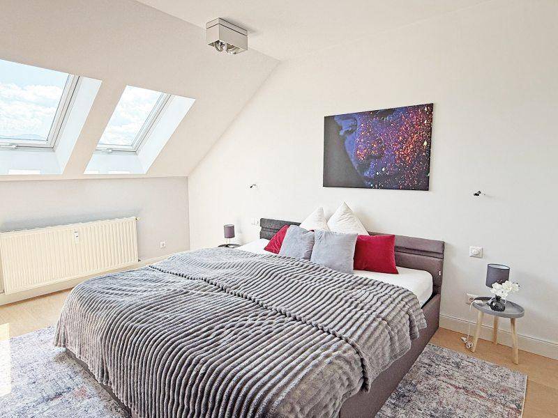Helles Schlafzimmer im Dachgeschoss mit mehreren Dachfenstern, schräger Decke und Holzboden.