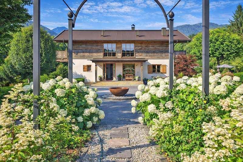 Elegante Hausfassade mit Holzelementen, umgeben von blühenden Hortensien und einem Steinweg.