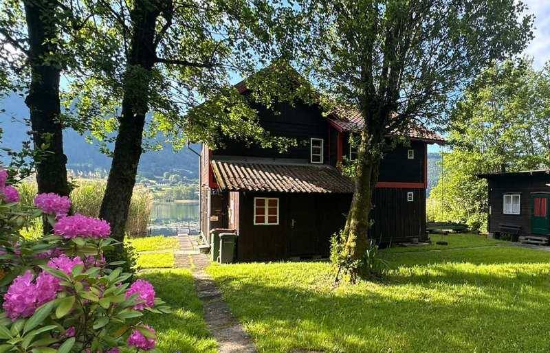 Das charmante Holzhaus ist von einem gepflegten Garten mit blühenden Rhododendren und hohen Bäumen umgeben.