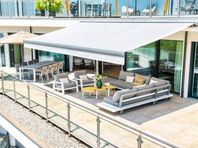 Großzügige Terrasse mit Ess- und Lounge-Bereich, geschützt durch eine Markise, ideal für Mahlzeiten im Freien.