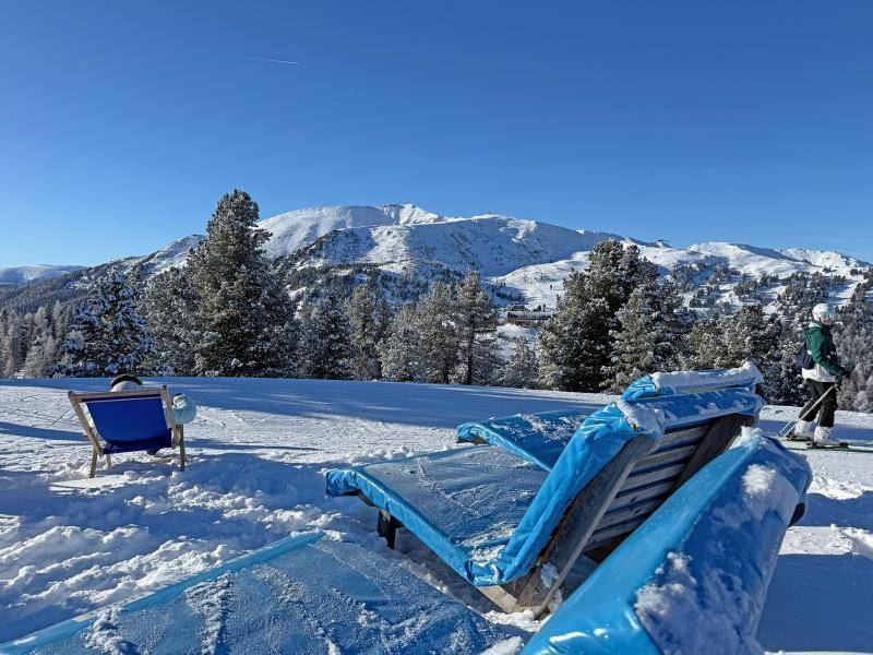 Entspannungsbereich im Schnee mit blauen Liegestühlen und einem atemberaubenden Blick auf die umliegende verschneite Bergwelt.