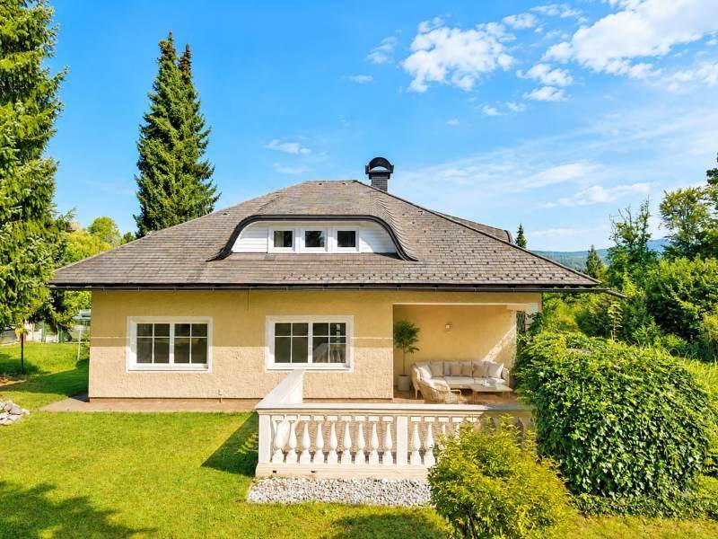 Hausfassade mit überdachter Terrasse und Sitzgelegenheiten im Grünen.