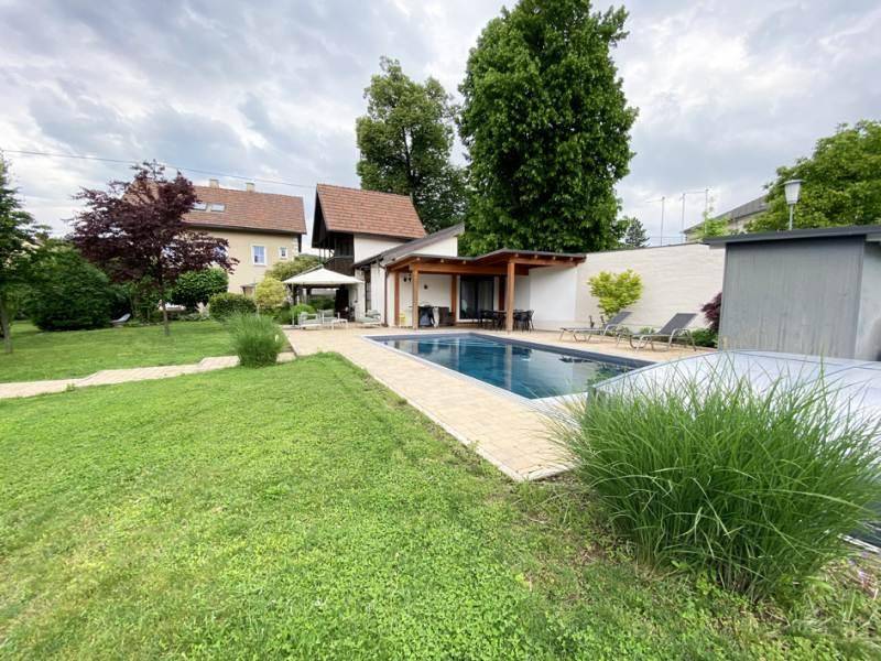 Weitläufiger Gartenbereich mit Pool, Liegewiese und Blick auf das Wohnhaus unter bewölktem Himmel.