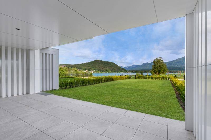 Überdachte Terrasse mit Fliesenboden und weitem Blick auf den See und die umliegende Berglandschaft.