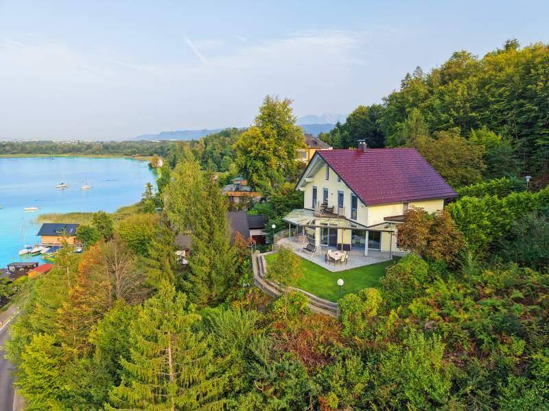Charmantes Haus mit rotem Dach und Terrasse, eingebettet in grüne Natur mit Seeblick.