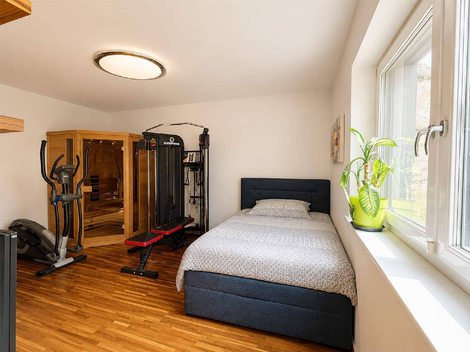 Schlafzimmer mit Fitnessgeräten, Sauna und großem Fenster für Tageslicht.