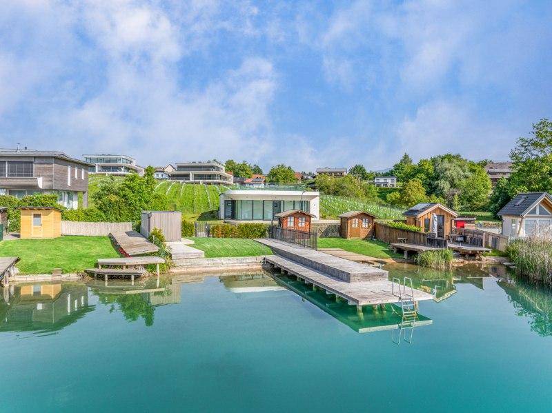 Malerische Seelandschaft mit privaten Stegen, kleinen Bootshäusern und grünen Gärten am Ufer.