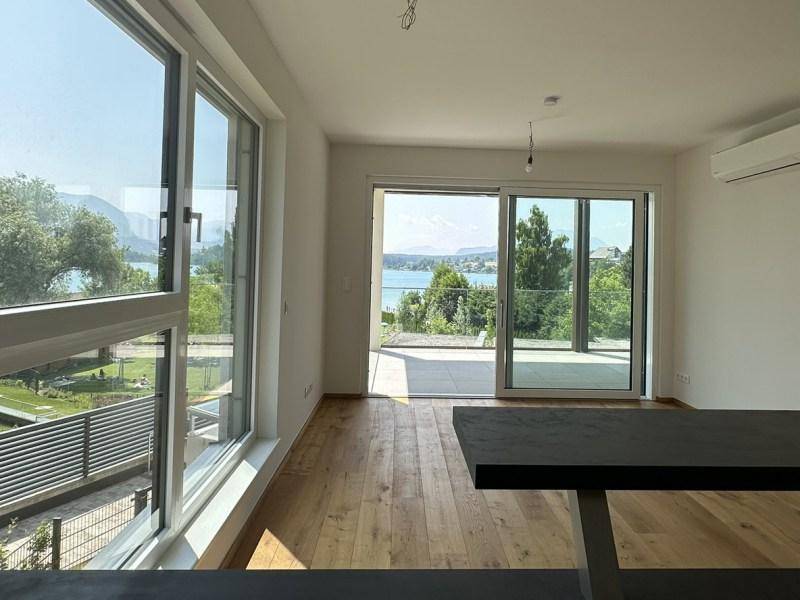 Lichtdurchfluteter Wohnraum mit Holzboden, großen Fenstern und Zugang zu einem Balkon mit Seeblick.