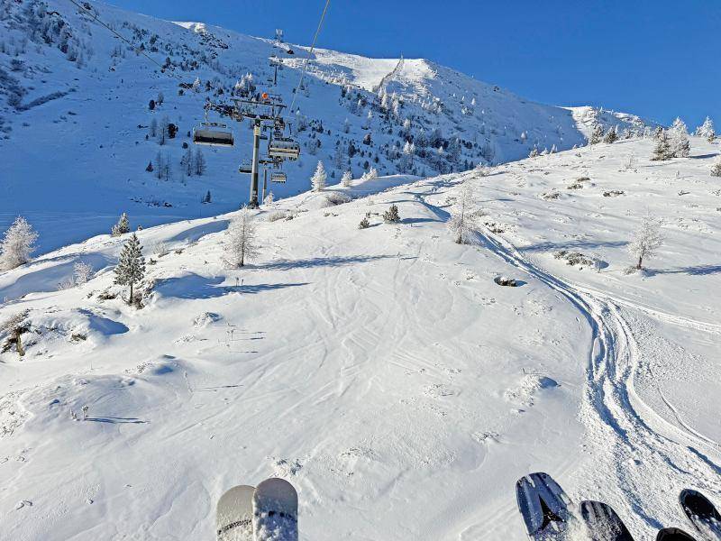 Blick vom Skilift auf eine verschneite Piste mit Spuren und majestätischen Bergen im Hintergrund.