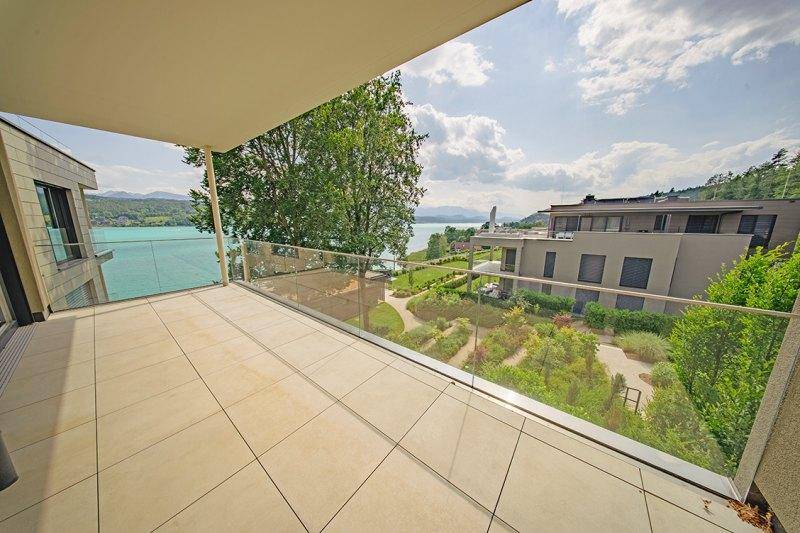 Moderner Balkon mit Glasbrüstung, der einen weiten Blick über die Wohnanlage und den See ermöglicht.