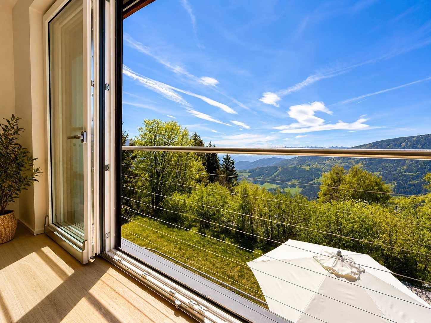 Große Falttüren öffnen sich zu einem Balkon mit weitem Blick über die grüne Berglandschaft.