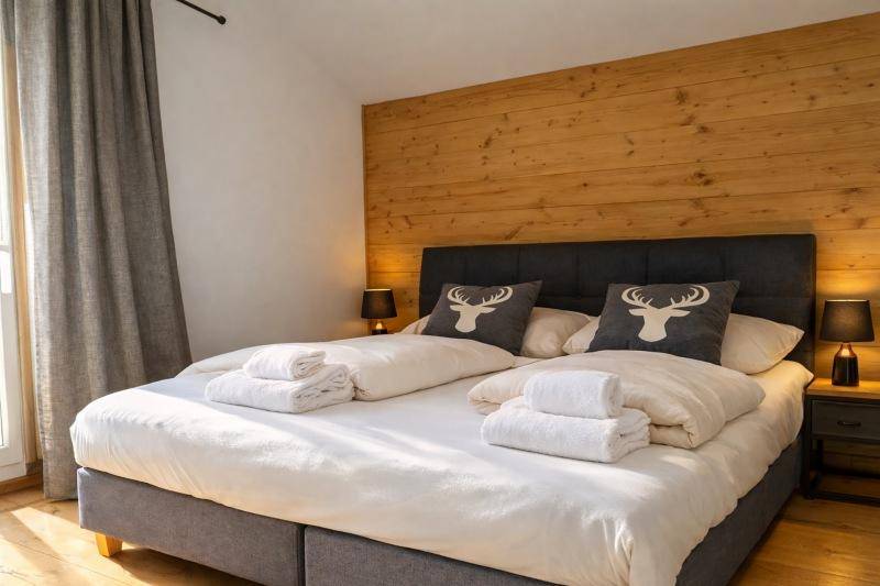 Gemütliches Schlafzimmer mit großem Doppelbett, Holzwand und Hirschmotiv-Kissen, ideal für alpine Nächte.