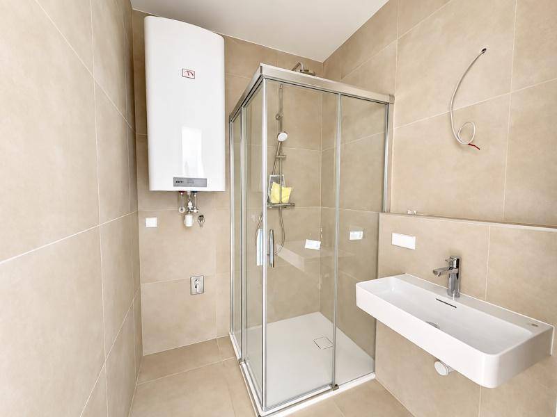 Modernes Badezimmer mit beigefarbenen Fliesen, Glasdusche und wandmontiertem Waschbecken.