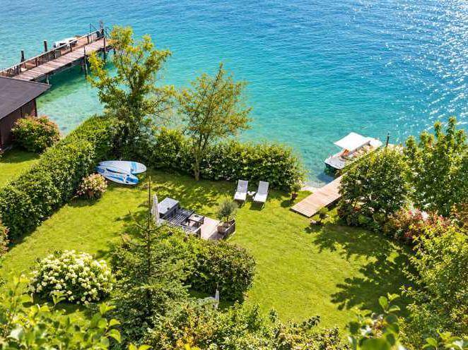 Idyllischer grüner Garten mit Terrasse und direktem Zugang zum See, inklusive privatem Steg und Liegeflächen am Ufer.