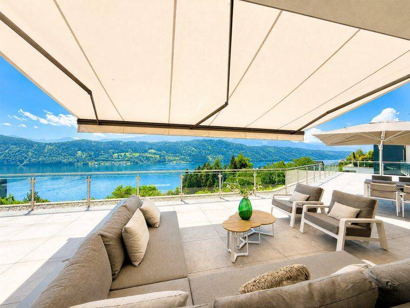 Weitläufige Terrasse mit Essbereich und Lounge-Möbeln, geschützt durch eine Markise, mit Panoramablick auf den See.