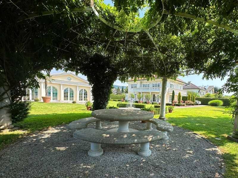 Gemütlicher Sitzbereich im Garten unter einer grünen Pergola mit Blick auf das Anwesen.