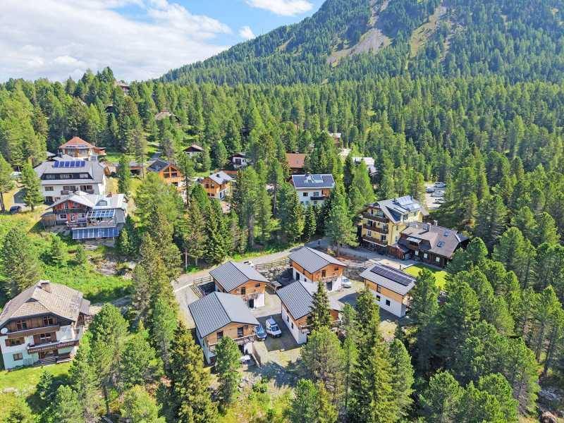 Nahaufnahme von modernen Chalets in einer bewaldeten Berglandschaft mit viel Grün.