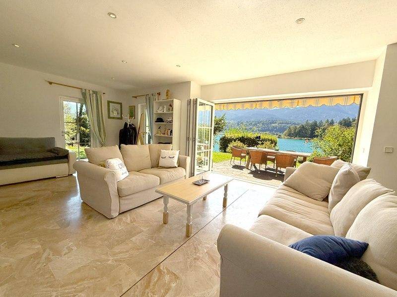 Helles Wohnzimmer mit beigem Sofa, Fliesenboden und direktem Zugang zur Terrasse mit Seeblick.