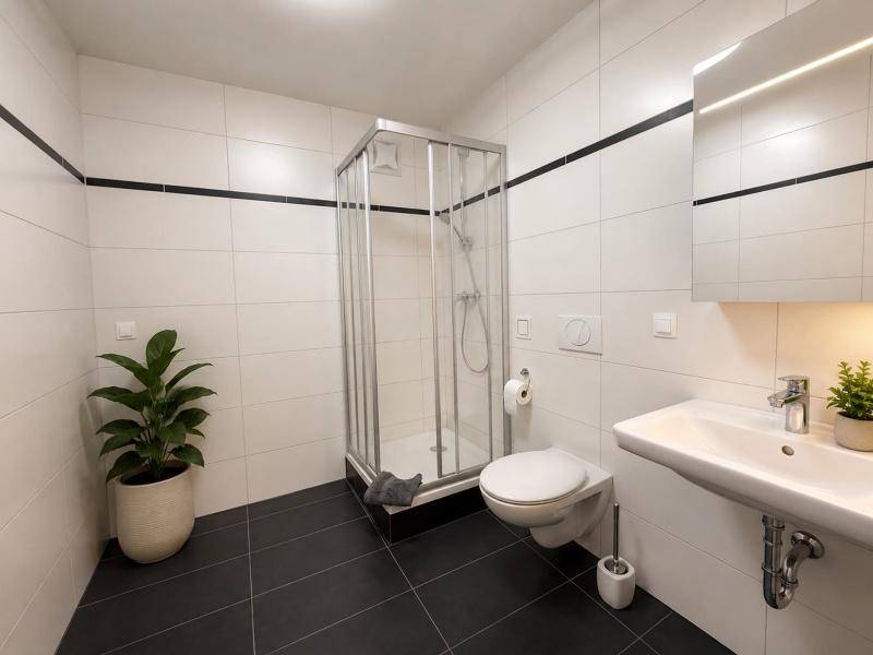 Modernes Badezimmer mit weißen und schwarzen Fliesen, Duschkabine und wandhängendem WC.