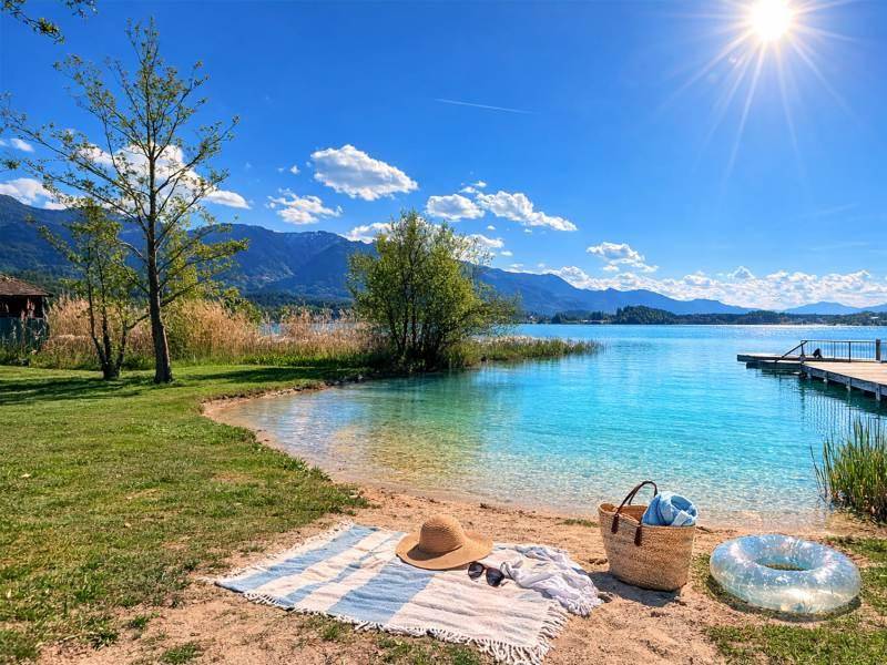 Sonniger Strandabschnitt am Seeufer mit Picknickdecke und Blick auf die umliegende Berglandschaft.