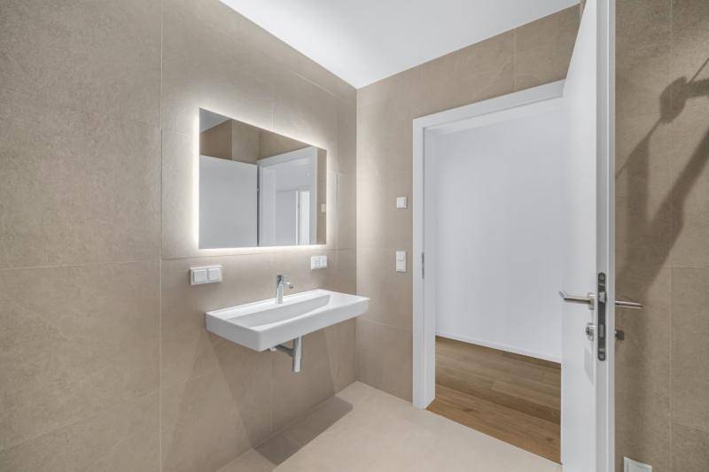 Modernes Badezimmer mit beigefarbenen Fliesen, beleuchtetem Spiegel und schwebendem Waschbecken.