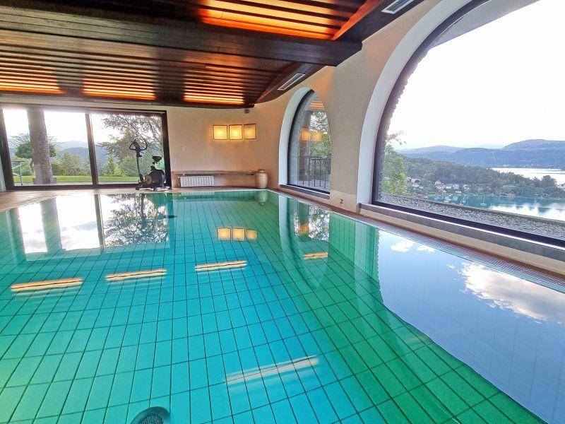 Innenpool mit weitem Seeblick durch große Panoramafenster und Holzbalkendecke.