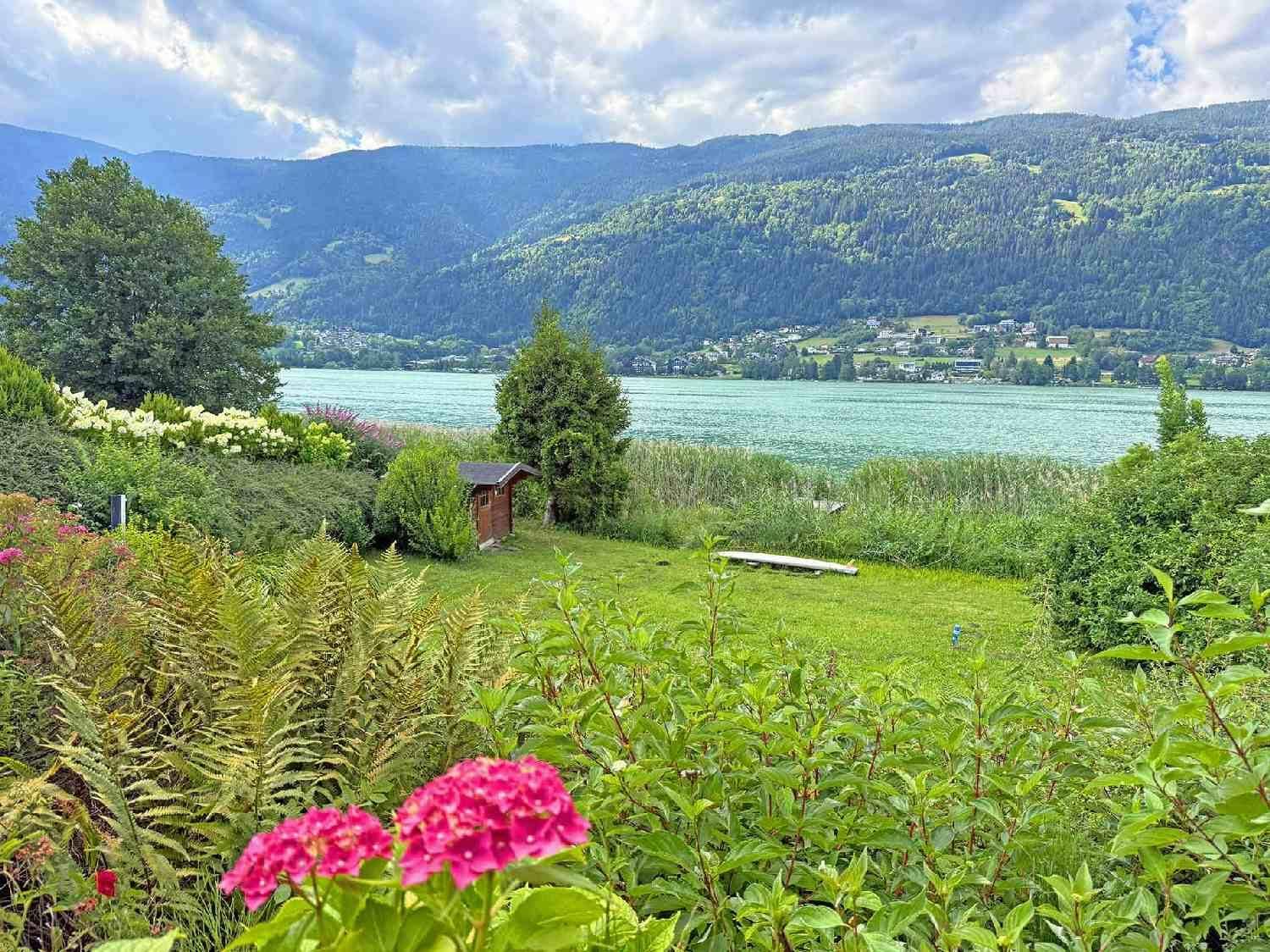 Weitläufiger Gartenbereich mit Rasenfläche, Blumen und einem kleinen Gartenhaus am Seeufer.