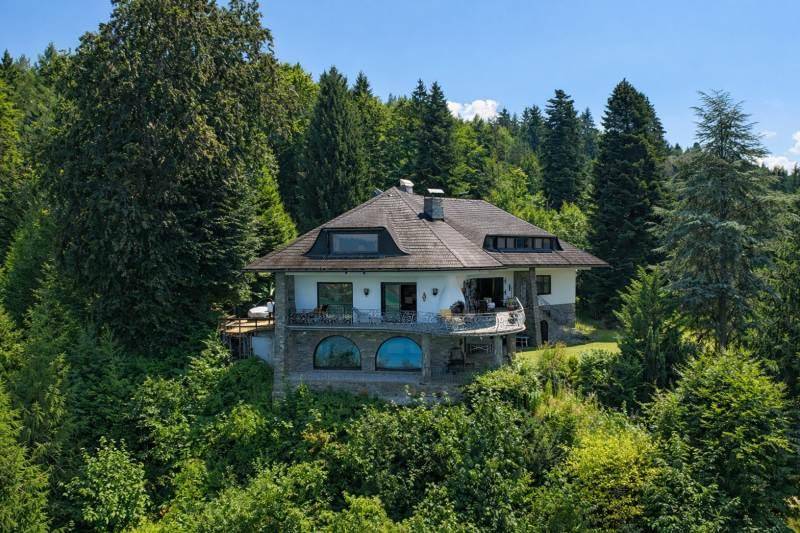 Elegantes Haus inmitten üppiger grüner Bäume, mit traditionellem Dach und Seeblick.