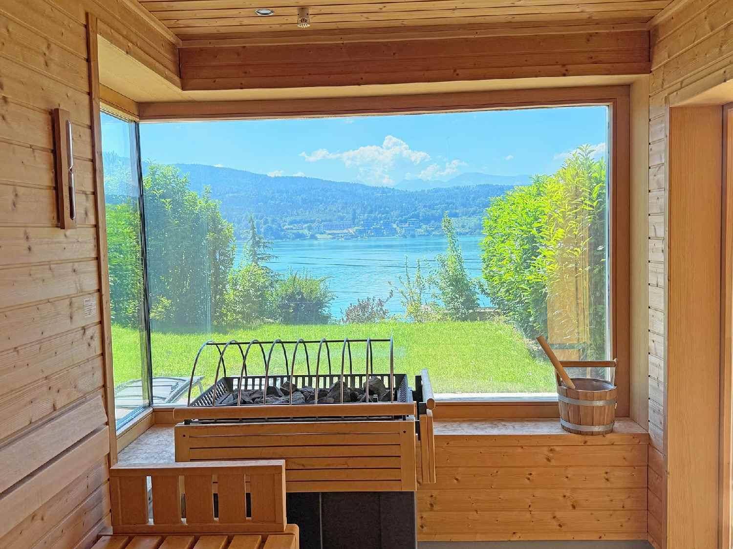 Sauna mit Holzbänken und großem Panoramafenster, das einen weiten Blick auf den See bietet.