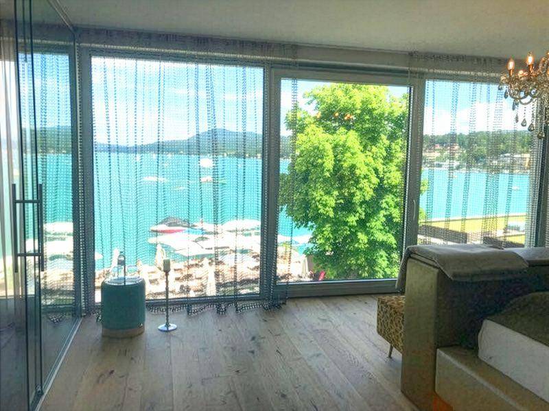 Helles Schlafzimmer mit großen Fenstern, Holzboden und direktem Blick auf den See.