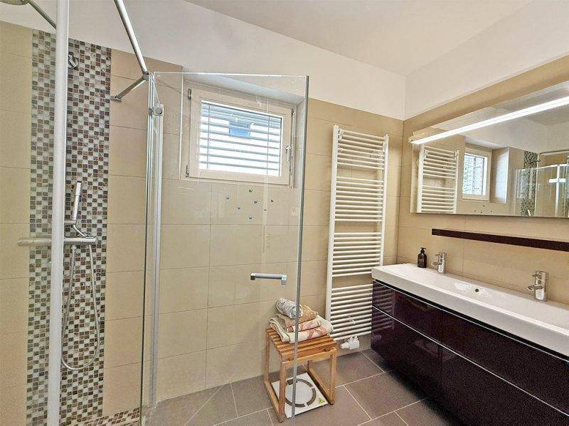 Modernes Badezimmer mit Doppelwaschbecken, großer Dusche und beheiztem Handtuchhalter.