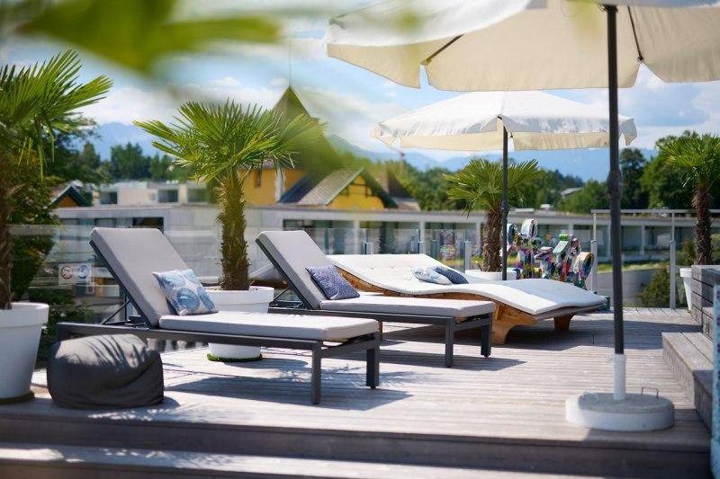 Sonniger Bereich auf der Dachterrasse mit Liegestühlen, Sonnenschirmen und Palmen.