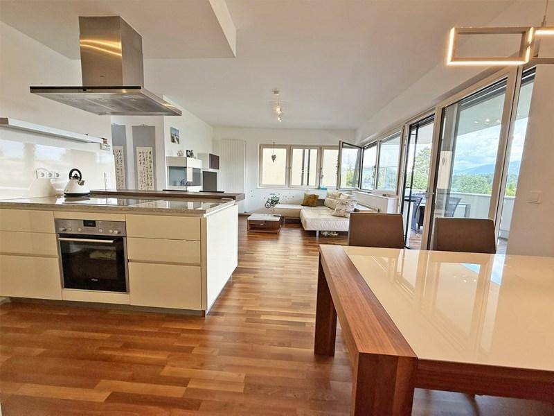 Heller offener Wohn-Essbereich mit moderner Küche, Holzboden und Zugang zum Balkon.
